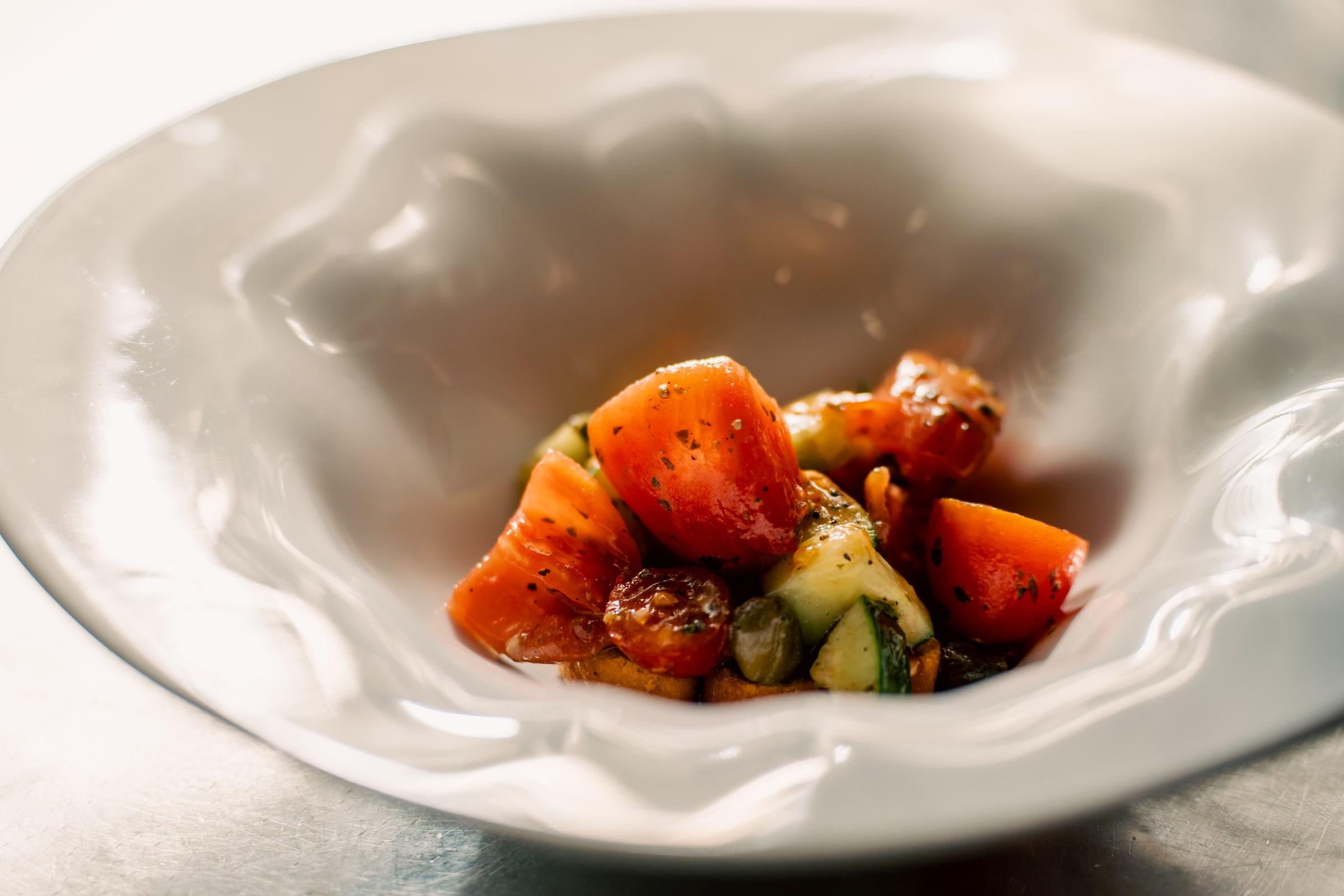 Tomato and cucumber salad in a white bowl, lit by the window