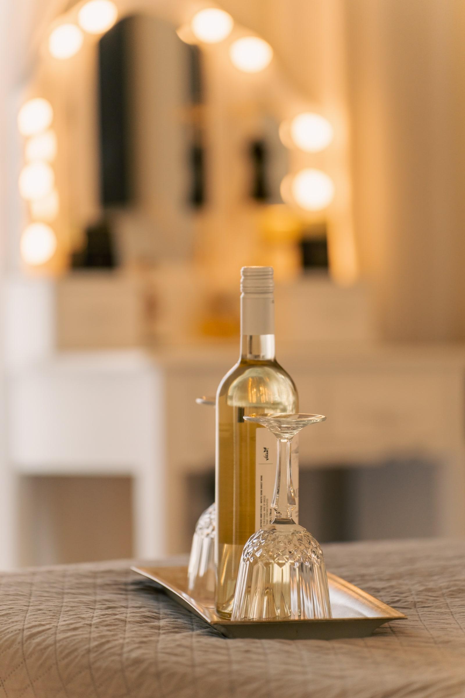 A bottle of white wine and two glasses set on the bed